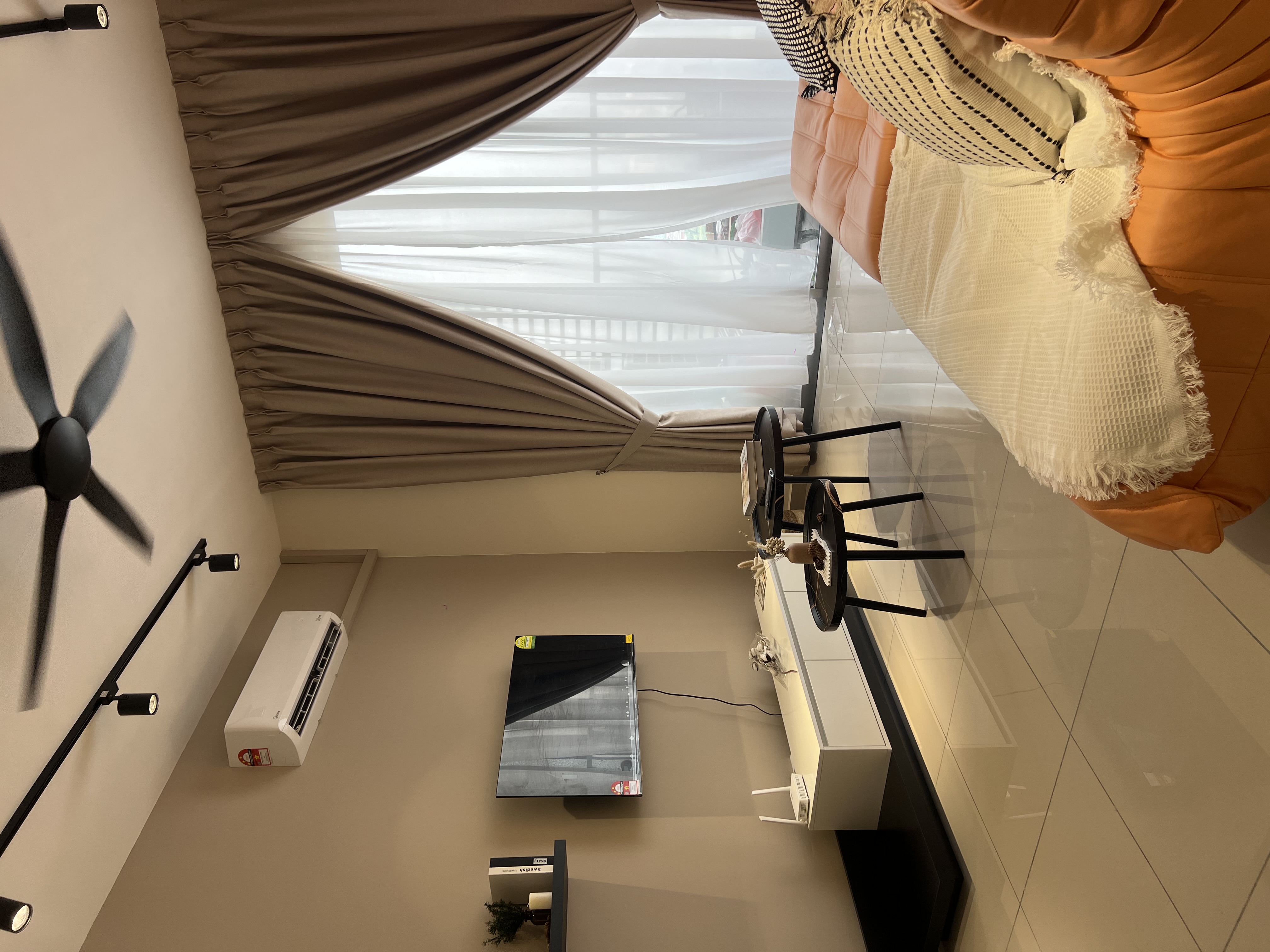 Styled living room — orange sofa, fan, TV, curtain